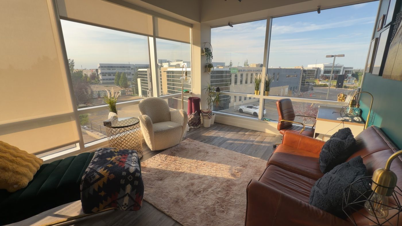 A bright corner seating area with a leather sofa, sheepskin armchair, plants and wide windows overlooking South Edmonton