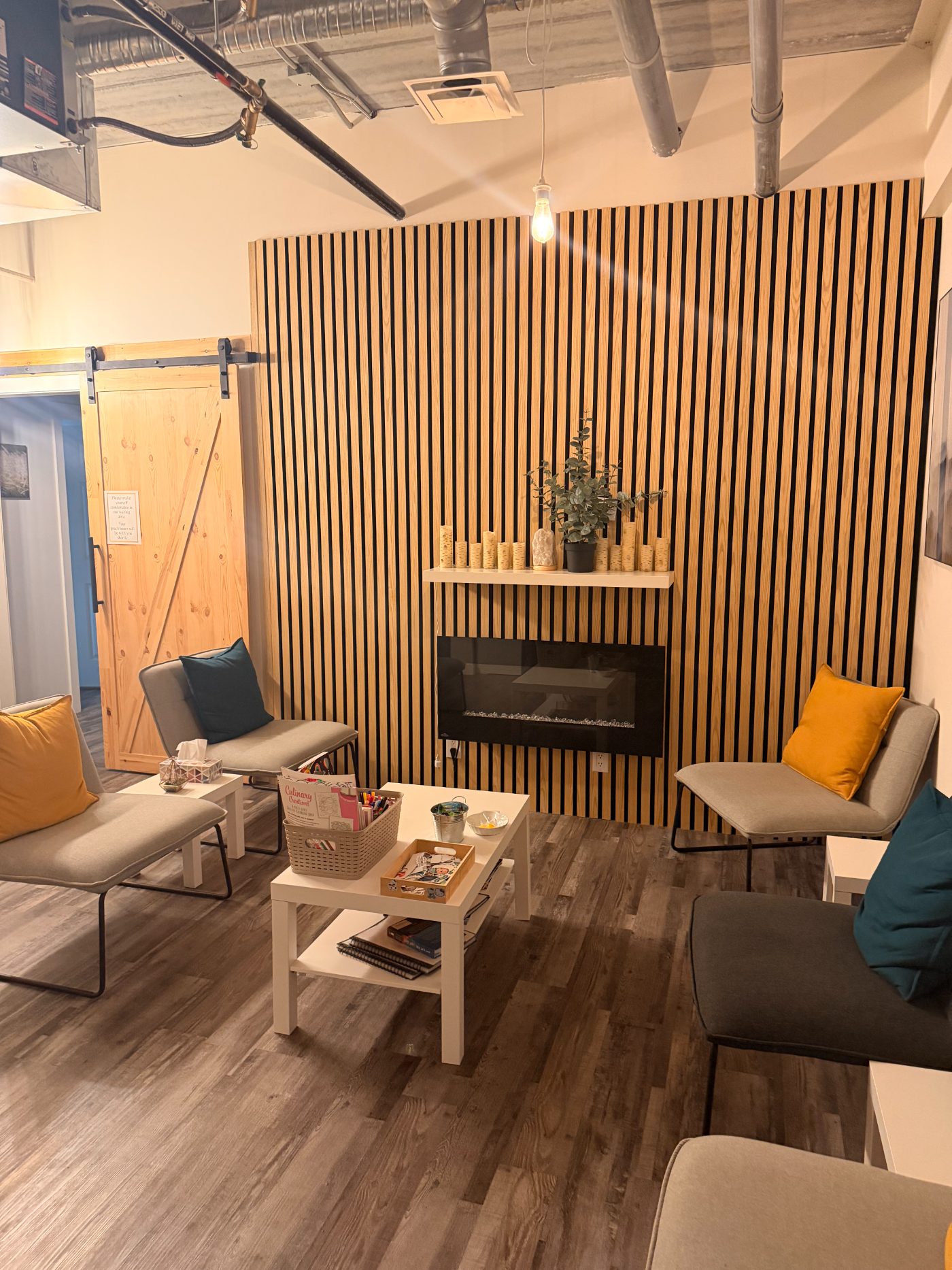 The shared waiting area, with soft armchairs, a slatted wood feature wall, a fireplace and a low table with colouring supplies